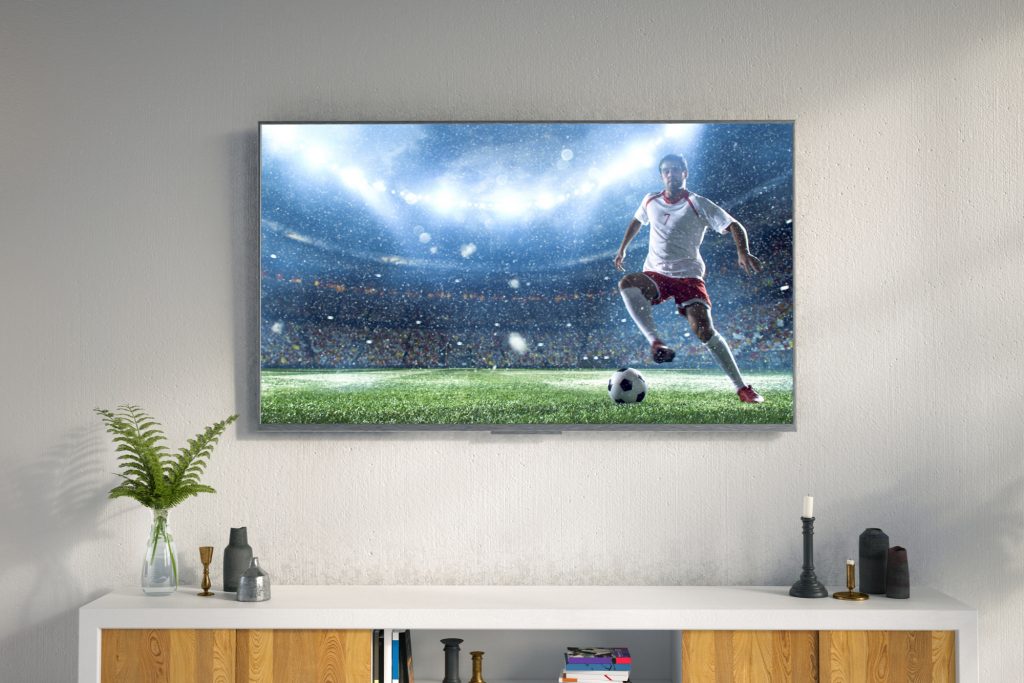 Wall-mounted TV above a media console showing a soccer match